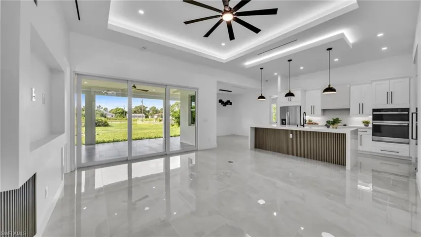 Unfurnished living room featuring ceiling fan, a tray ceiling, light marble finish floors, and recessed lighting