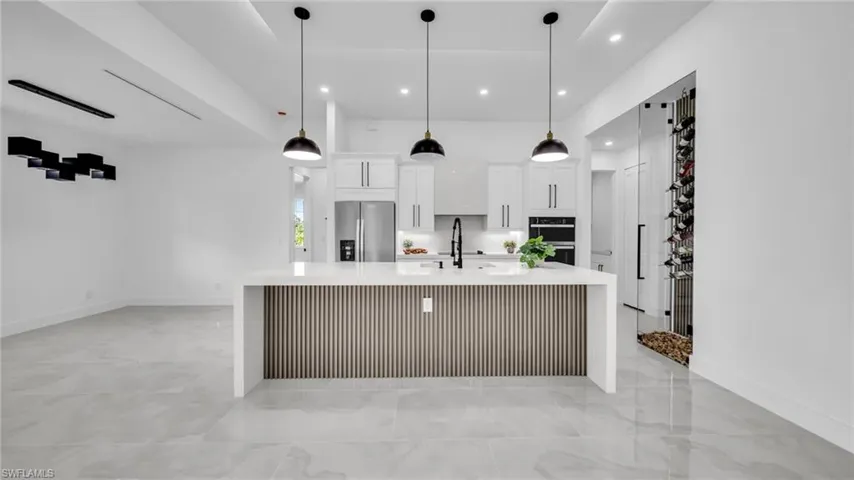 Kitchen with light countertops, white cabinets, a large island, stainless steel fridge, and recessed lighting