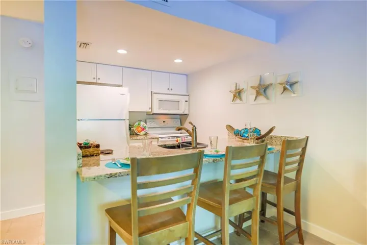 Kitchen with light stone counters, white appliances, white cabinets, a kitchen breakfast bar, and recessed lighting