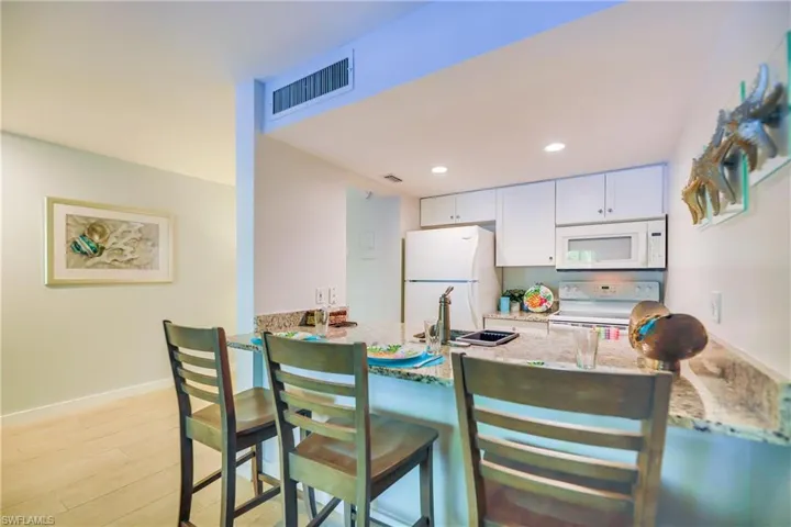 Kitchen with a breakfast bar, white cabinetry, light stone counters, white appliances, and recessed lighting