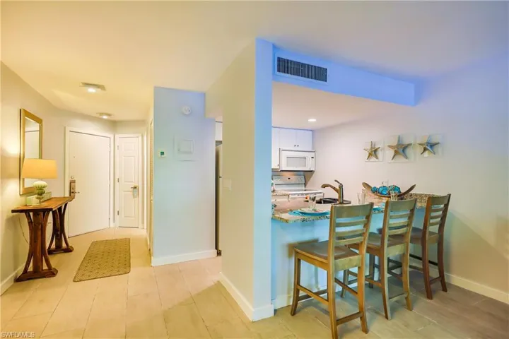 Kitchen featuring a kitchen breakfast bar, white cabinets, a peninsula, white appliances, and light stone countertops