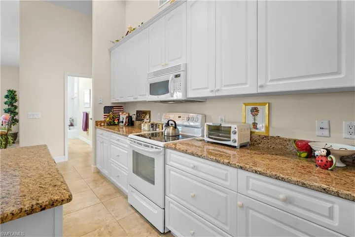 Big kitchen with white appliances, white 42" high cabinets with crown molding, light stone counters, and a towering ceiling. Lots of counter space a cooks dream!