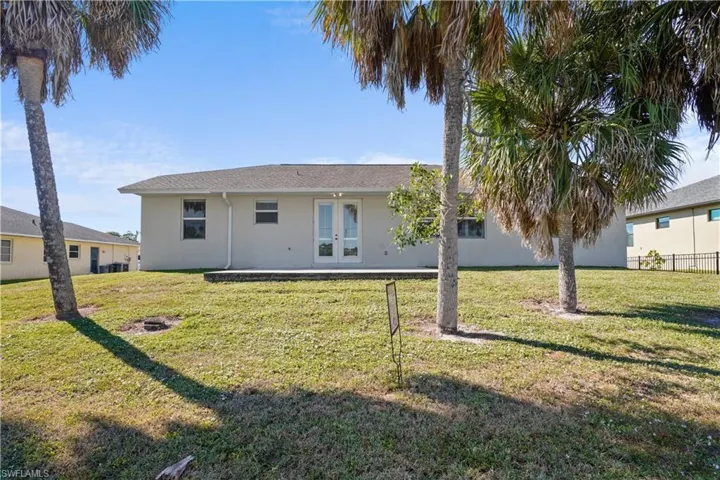 Rear view of property with a lawn, french doors, a patio area, and stucco siding.