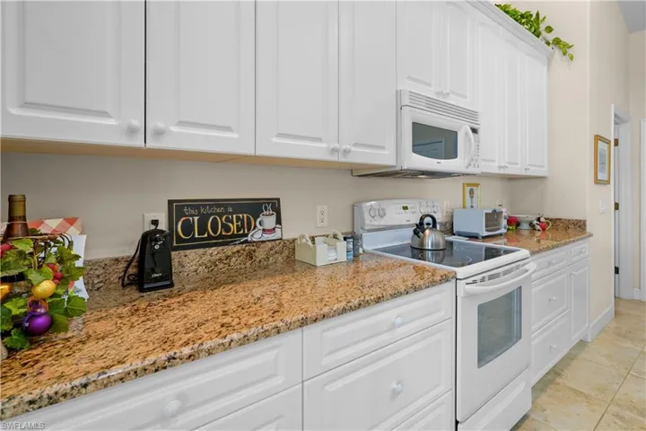 Beautiful kitchen with white appliances, including built-in microwave, tons of counter space and cabinetry storage! The granite countertops and 42" high white cabinets, 20"  porcelain tile.