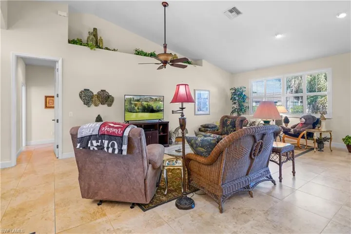Living room with high vaulted ceiling, ceiling fan, and light tile patterned flooring and plant shelves.