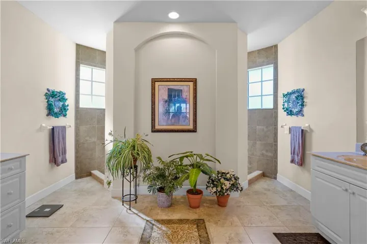 Spacious bathroom with two seperate vanities, a walk though shower, healthy amount of natural light, and light tile patterned flooring.