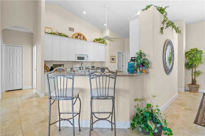 Kitchen with 42" high white cabinetry, beautiful granite countertops, breakfast bar that opens to the great room, arched walkways, to the guest rooms, high vaulted ceiling, and light nutral colored porcline 20" tile looring.