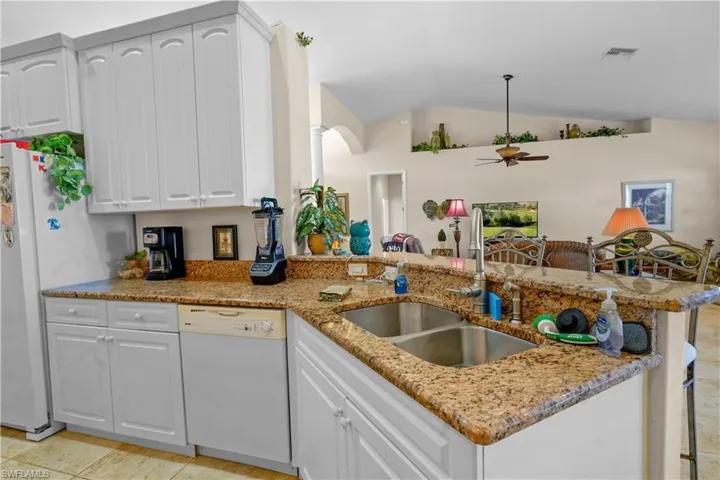 Kitchen with a peninsula, white dishwasher, vaulted ceiling, white 42 " high cabinets with crown molding, and granite high breakfast bar over looks the great room..