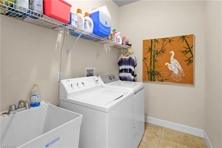 Washroom featuring washing machine, clothes dryer, laundry tub and shelf for supplies and hanging items to dry. The 20" porcelain tile is throughout the the home.
