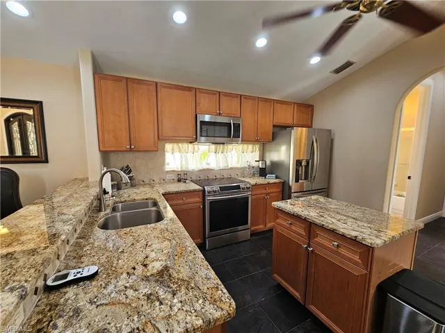 Kitchen with brown cabinets, stainless steel appliances, arched walkways, a center island, and decorative backsplash
