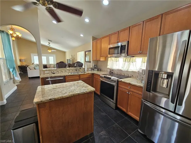 Kitchen featuring stainless steel appliances, open floor plan, a peninsula, lofted ceiling, and light stone countertops