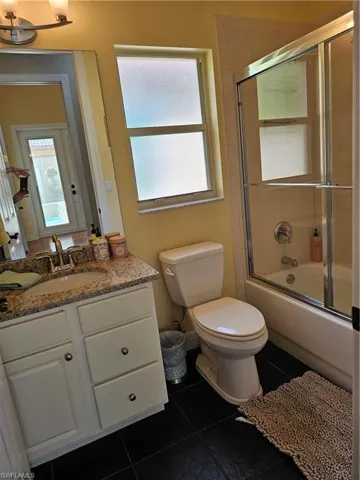 Bathroom with bath / shower combo with glass door, plenty of natural light, vanity, and dark tile patterned floors