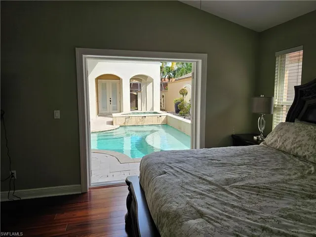 Bedroom with dark wood-style flooring, lofted ceiling, and arched walkways