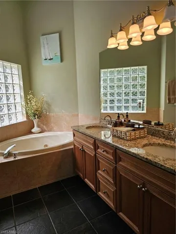 Full bathroom featuring a whirlpool tub, double vanity, and dark tile patterned flooring