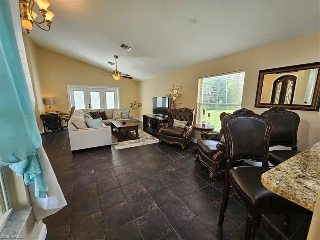 Living room featuring vaulted ceiling, ceiling fan, a chandelier, and dark stone finish flooring