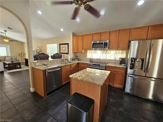 Kitchen featuring open floor plan, ceiling fan, stainless steel appliances, light stone counters, and recessed lighting