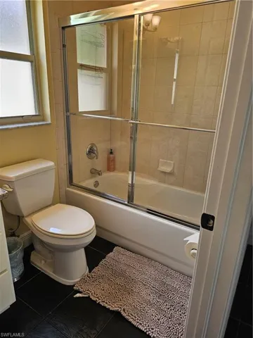 Full bath featuring bath / shower combo with glass door and dark tile patterned flooring
