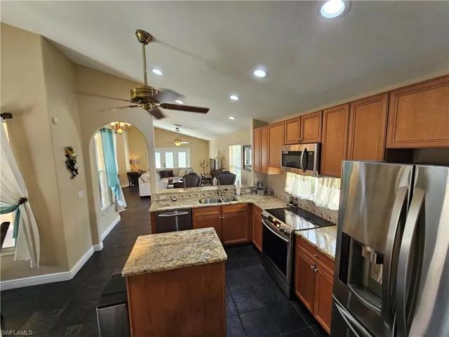 Kitchen featuring open floor plan, stainless steel appliances, a peninsula, lofted ceiling, and light stone countertops