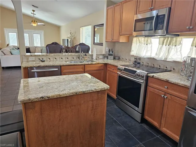 Kitchen with open floor plan, appliances with stainless steel finishes, a ceiling fan, a peninsula, and vaulted ceiling