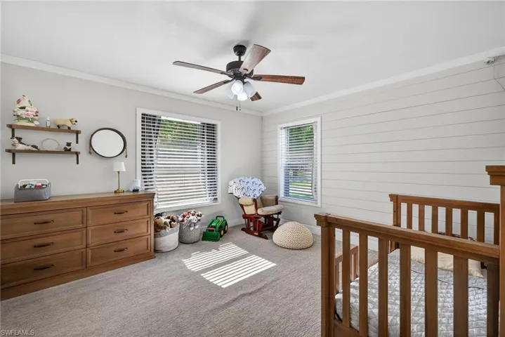 Bedroom featuring ornamental molding, a nursery area, wooden walls, carpet flooring, and a ceiling fan