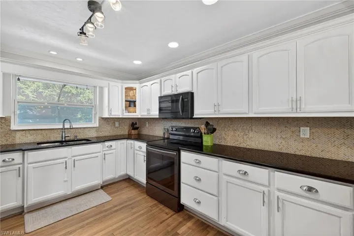 Kitchen with electric range oven, white cabinets, black microwave, light wood finished floors, and decorative backsplash