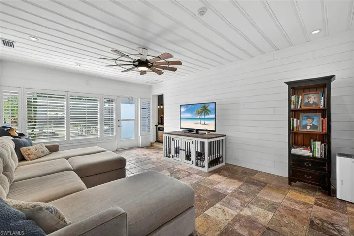 Living area featuring wooden walls, recessed lighting, a ceiling fan, and stone tile floors