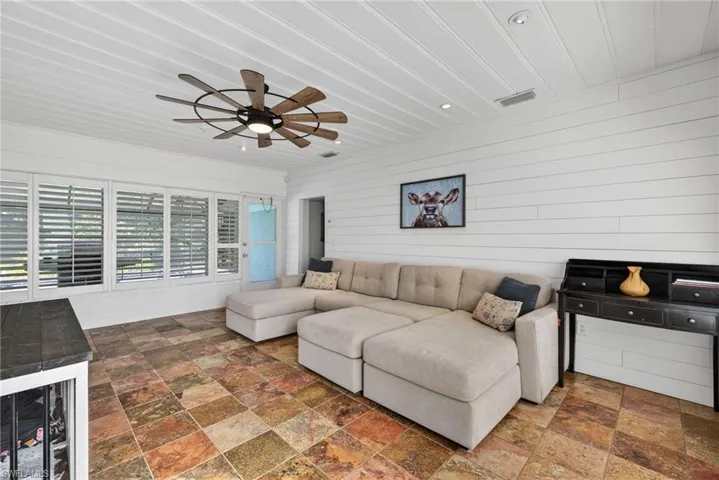 Living area with wooden walls, stone tile floors, ceiling fan, and wine cooler