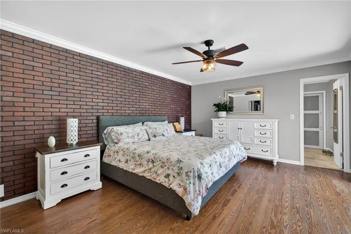 Bedroom featuring brick wall, crown molding, an accent wall, dark wood-style flooring, and a ceiling fan