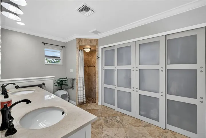 Bathroom featuring tiled shower, crown molding, double vanity, and stone tile floors