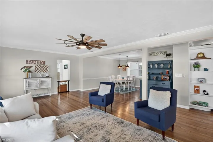Living area with dark wood finished floors, built in features, ceiling fan, and ornamental molding