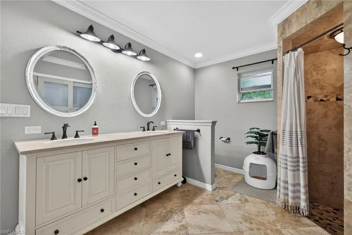 Full bathroom with tiled shower, double vanity, ornamental molding, and a textured wall