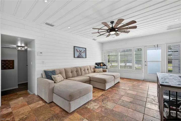 Living area featuring wood walls, a ceiling fan, stone tile flooring, and recessed lighting