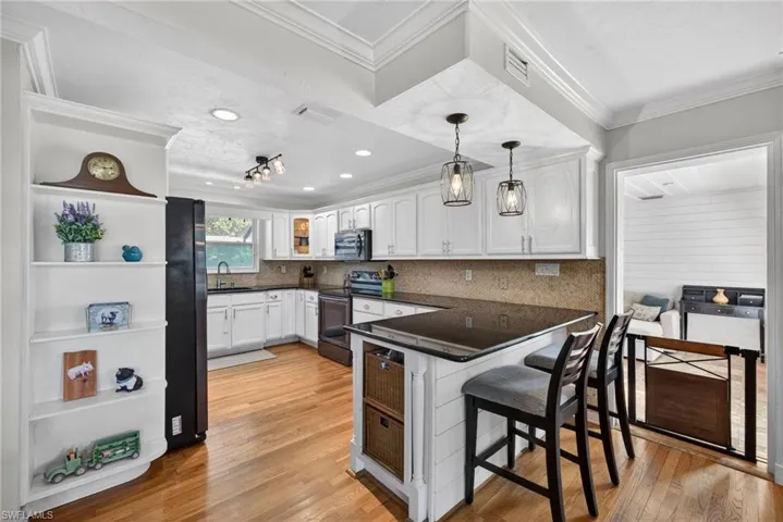 Kitchen with white cabinetry, pendant lighting, a kitchen breakfast bar, stainless steel appliances, and crown molding