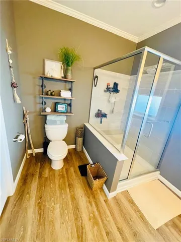 Bathroom with toilet, an enclosed shower, ornamental molding, and hardwood / wood-style flooring