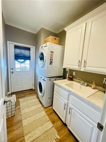 Clothes washing area with sink, stacked washer / drying machine, light hardwood / wood-style flooring, and cabinets