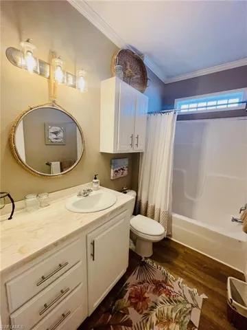 Full bathroom with wood-type flooring, shower / tub combo, toilet, vanity, and ornamental molding
