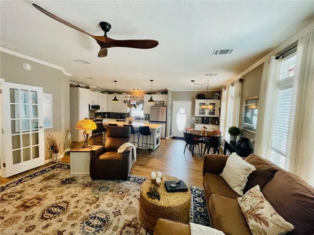Living room featuring ceiling fan with notable chandelier, crown molding, a textured ceiling, and light hardwood / wood-style floors