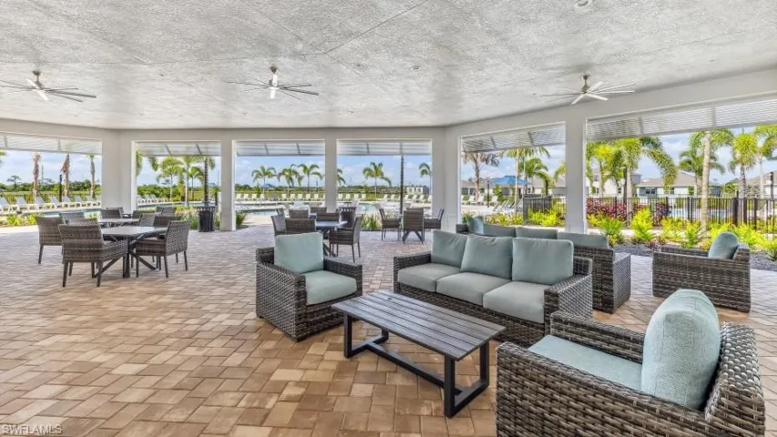 The property offers an expansive covered outdoor patio with a textured ceiling and ceiling fans, featuring comfortable seating arrangements and paved flooring