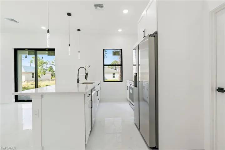 Kitchen featuring white cabinets, stainless steel refrigerator with ice dispenser, sink, hanging light fixtures, and a kitchen island with sink