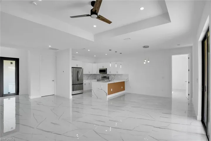 Open-concept kitchen featuring a center island with stone-finish waterfall edges, white shaker-style cabinetry, stainless steel appliances, recessed ceiling lighting, and polished stone-finish flooring