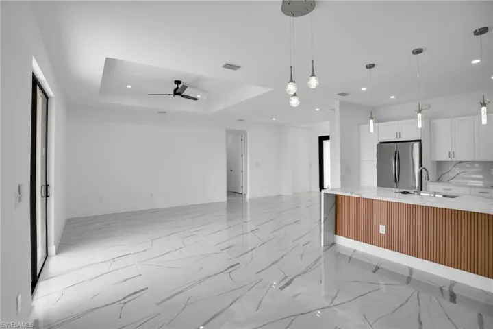 Open-concept interior featuring large-format tile flooring with marble-pattern veining, a recessed tray ceiling with a central fan, and a kitchen island with a fluted wood-finish panel