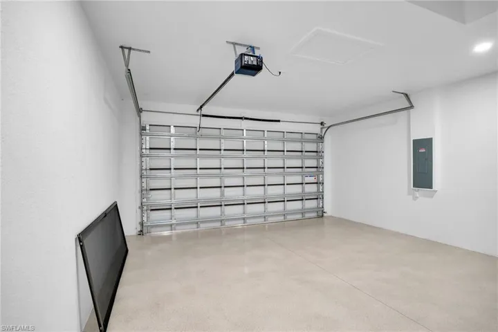 Enclosed garage featuring finished concrete flooring, painted walls, overhead lighting, and an automated door opener mechanism