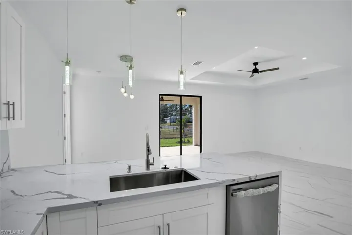 Kitchen island featuring a stone-look countertop with an undermount stainless steel sink, sleek pendant lighting, white cabinetry, and tray ceiling with an integrated ceiling fan