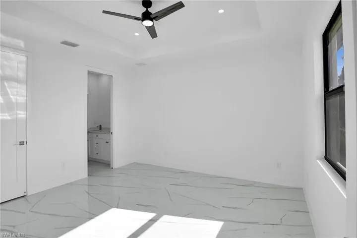 Tray ceiling with recessed lighting, large-format tile flooring with veined pattern, matte black ceiling fan, and black-framed windows