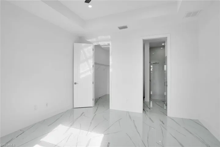Polished stone-finish flooring with gray veining, tray ceiling, recessed lighting, and solid-core interior doors