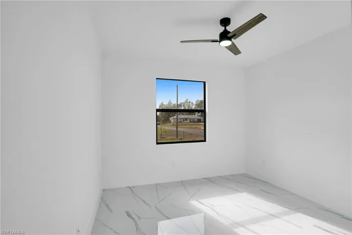Neutral interior room featuring large-format tile flooring with veining detail, matte black window casing, and a modern three-blade ceiling fan with integrated lighting