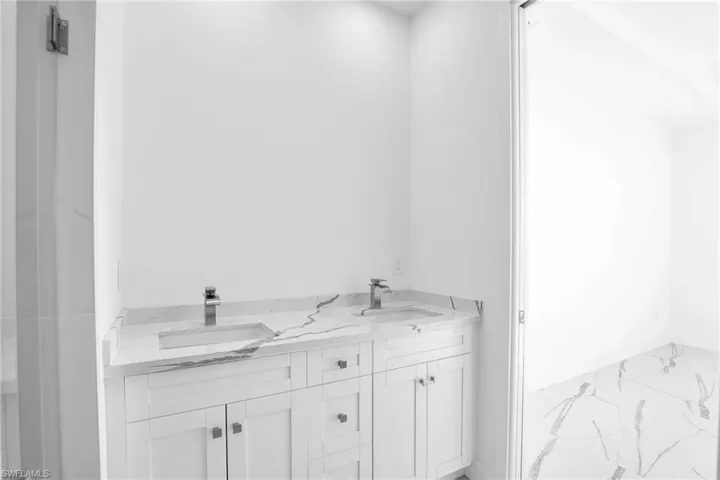 Dual-sink vanity featuring stone-patterned countertops, integrated rectangular basins, polished metallic hardware, and white Shaker-style cabinetry