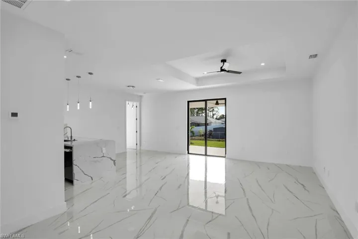 Open-concept interior featuring large-format tile flooring with a veined pattern, tray ceiling with a matte black ceiling fan, kitchen island with stone-finish waterfall countertop, and sliding glass doors