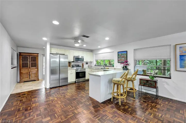Kitchen with stainless steel appliances, white cabinetry,  kitchen peninsula, ceiling fan and hallway to side lanai entrance.