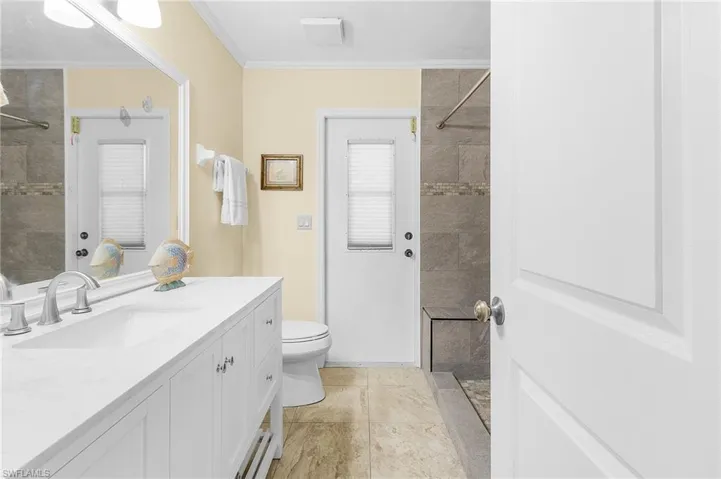 Bathroom with toilet, crown molding, a tile shower, tile patterned floors, and vanity